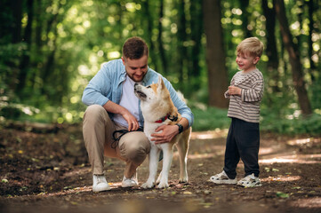 Boy is laughing. Father with son and dog are in the forest