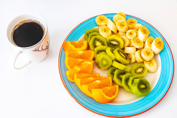 Sliced oranges kiwi and bananas on a plate and coffee.