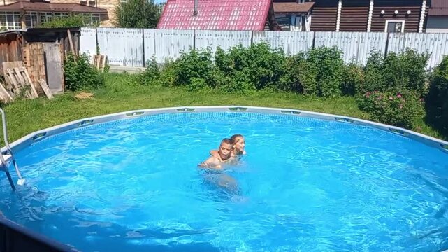 Two kids brother and sister playing in pool in backyard on sunny day, top view