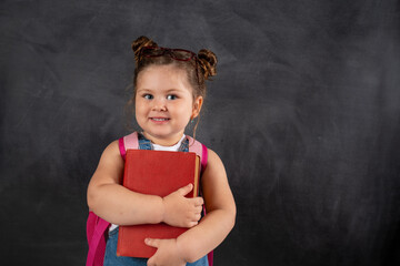 Cute little school girl with book smiling on black chalkboard.