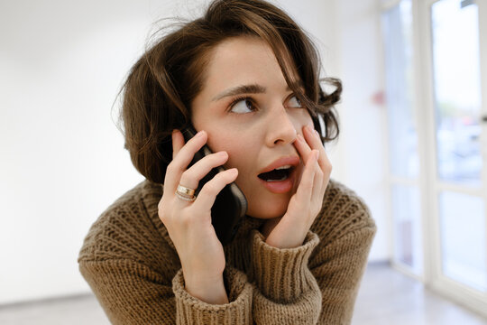 Person showing a shocked expression while talking on a phone indoors.