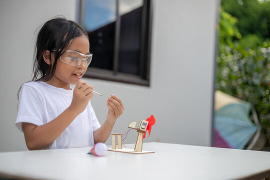 A young girl explores renewable energy outdoors by playing with a wind turbine toy - Powered by Adobe