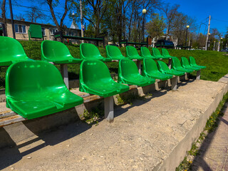 A row of green chairs are lined up on a sandy area. The chairs are empty and the area is empty