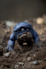 Obraz premium A blue monster with three eyes and a mouth is standing in the dirt. The monster appears to be dirty and tired, and it seems to be looking up at the camera
