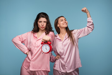 Two cheerful women wearing matching pink pajamas celebrating their morning energy while holding an...