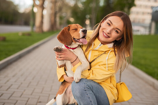 Cheerful woman hugging her beagle dog in an outdoor park setting, enjoying the sunny day.