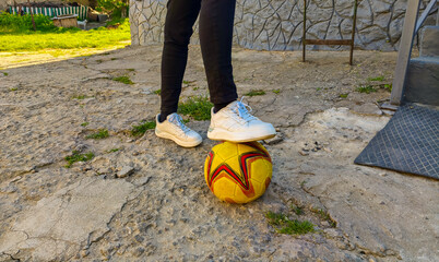 A person is standing on a soccer ball in a yard. The person is wearing white shoes and black pants