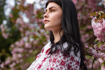Naklejka premium A portrait of a young woman in traditional clothing surrounded by vibrant pink cherry blossoms, showcasing nature's beauty and cultural elegance.