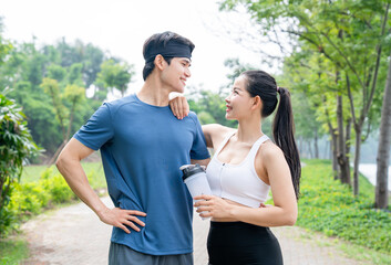 Athletic couple smiles on trail after outdoor exercise holding protein shake in a scenic park