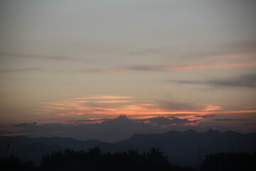 Sunset over a mountainous landscape with a silhouetted foreground of trees.