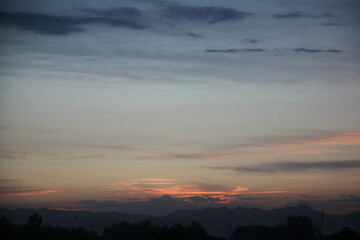 Sunset over a mountainous landscape with a silhouetted foreground of trees.