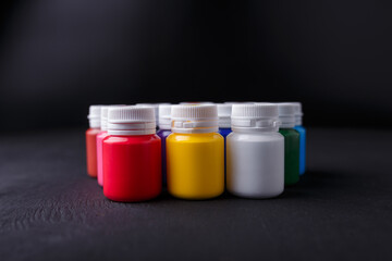 Small bottles of multicolored acrylic or gouache paint jars in a box on dark background. Art materials. Copy space