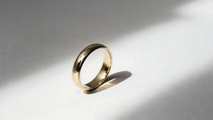 A single gold wedding ring rests on a bright white surface, casting a shadow.