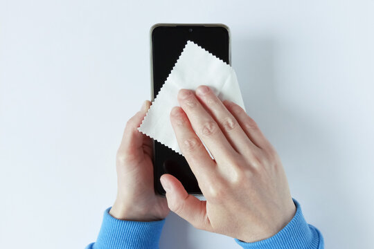 Caucasian woman wipes napkin smartphone screen with lint-free cloth holding it in her hands. White background.