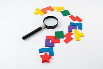 Concept of uncertainty, problem solving, or search for answers. Symbolized by question mark crafted from unsolved colorful block puzzle with magnifying glass in the center 
