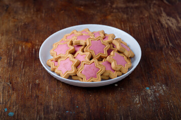 Star shaped cookies with pink frosting on white plate, wooden rustic background. Strawberry icing on cookies in shape of stars. Closeup
