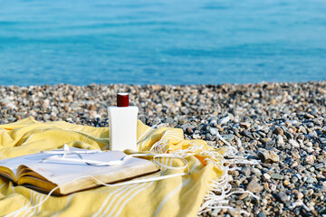 Summertime mood. Audiobook or podcast during summer holidays. Headphones, book and sunscreen no yellow blanket for relaxing on the beach.
