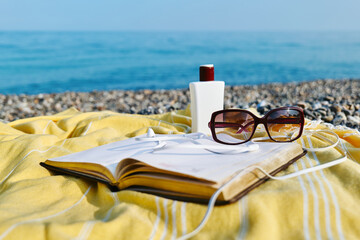Summertime mood. Audiobook or podcast during summer holidays. Headphones, open book, sunglasses and sunscreen no yellow blanket for relaxing on the beach.