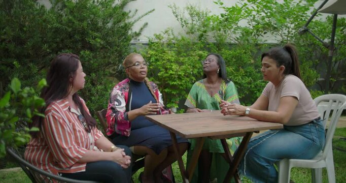 One woman shares animated thoughts while others listen attentively during lively group exchange in leafy backyard garden setting