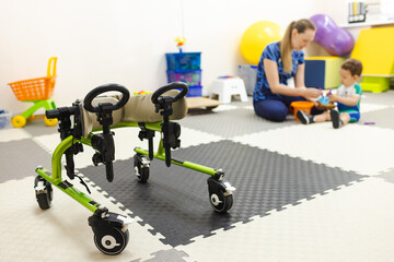 Rehab walkers for young boy with movement disorders who, in the background, is rehabilitating with a physical therapist