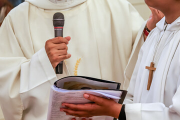 Cérémonie de baptême ou communion dans une église catholique : prêtre lisant un livret liturgique avec un enfant en aube et croix chrétienne