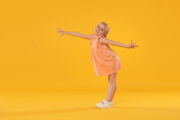 Cute little girl dancing on orange background
