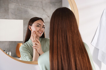 Beautiful woman looking at herself in mirror indoors