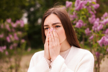 Woman suffering from seasonal pollen allergy near blossoming shrub on spring day