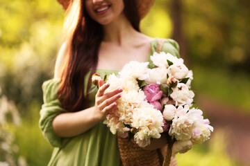 Fototapeta premium Beautiful woman with bouquet of peonies in park, closeup
