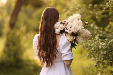 Beautiful woman with bouquet of peonies in park, back view © New Africa