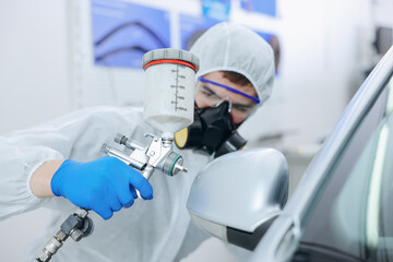 Worker painting car in body shop, selective focus