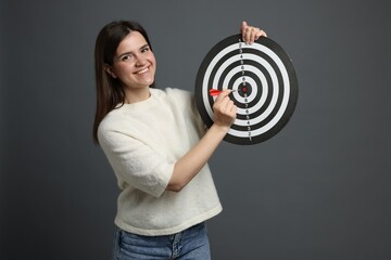 Targeting. Smiling woman with dart board and arrow on grey background