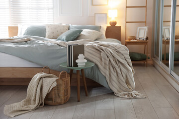 Comfortable bed with soft linens, lamp and decor in stylish room. Home textile