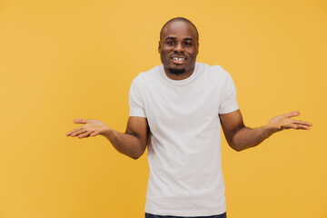 Young man shrugging shoulders expressing doubt on yellow background