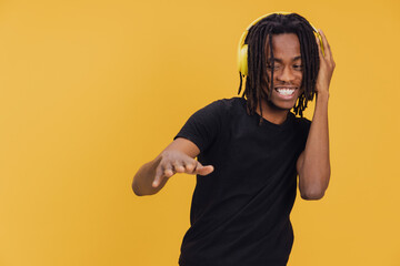 Young man enjoying music with yellow headphones on yellow background