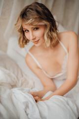 Fototapeta premium Beautiful young woman in a white dress on white sheets