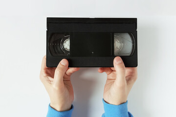 Black video cassette in hands of Caucasian woman. White background. Top view.