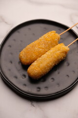 A corn dog is a hot dog on a stick that has been coated in a thick layer of cornmeal batter and deep fried. corn dod on black plate
