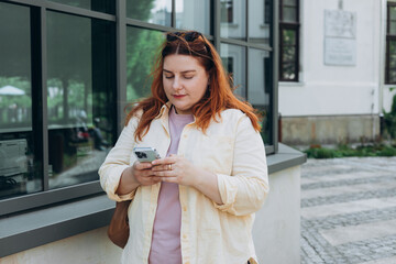 Happy redhead woman using phone walking in city street. Lifestyle, travel, tourism, technology, blogging, communication concept. High quality photo