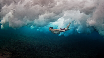 Man dives and swims underwater under the breaking wave