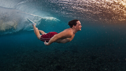Man dives and swims underwater under the breaking wave