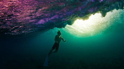 Man dives and swims underwater under the breaking wave