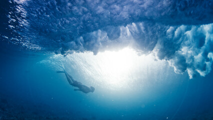 Man dives and swims underwater under the breaking wave