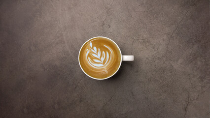 Top view of hot cafe latte coffee in white cup with beautiful latter art on grunge look cement table.