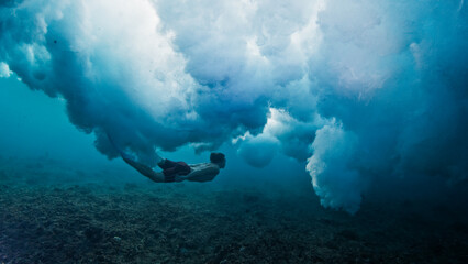 Man dives and swims underwater under the breaking wave