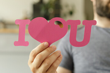 Close-up of a man's hand holding a paper cutout that says 'I love you'.