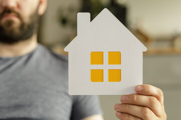 A man holds a paper house cutout, symbolizing homeownership, real estate, or new home purchase.
