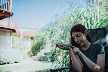 A young woman interacts with a lizard in a sunny outdoor setting, highlighting a moment of...