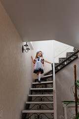 A cute schoolgirl in a school uniform goes down the stairs in the house.