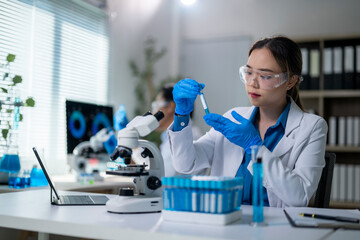 A woman in a lab coat is holding a test tube and wearing safety goggles